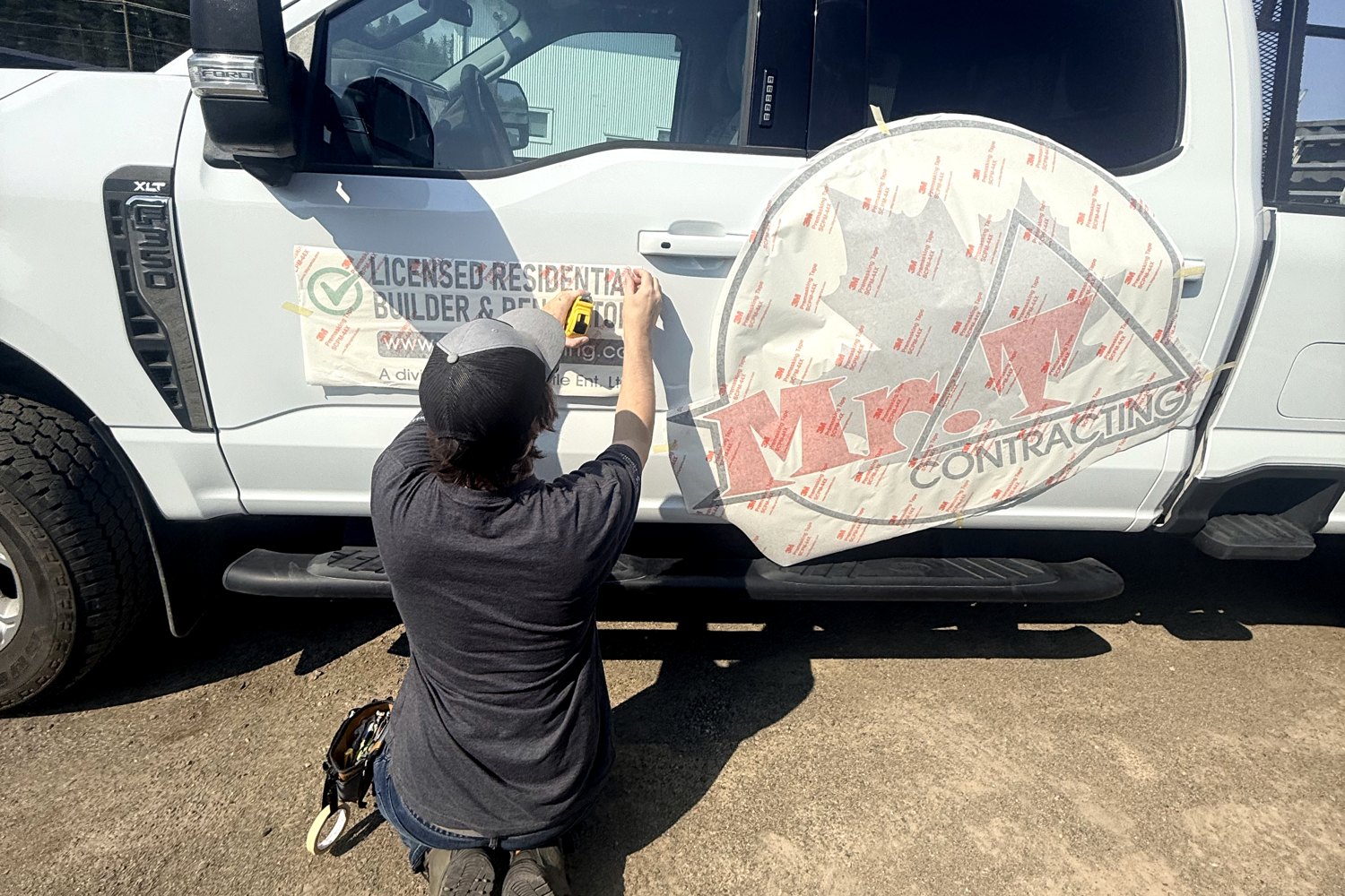 Liam at a truck door, squaring up a Mr. T Contracting graphic still under application tape.