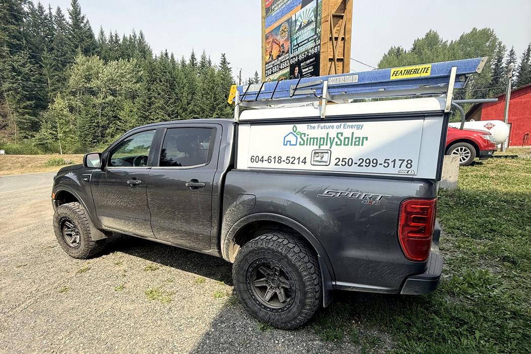 Simply Solar service truck with canopy graphics, parked by a Cariboo roadside board.