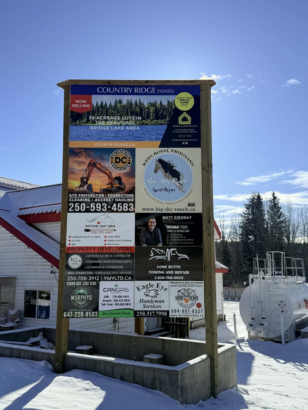 A multi-panel roadside signboard near Bridge Lake carrying advertising for a dozen local businesses.