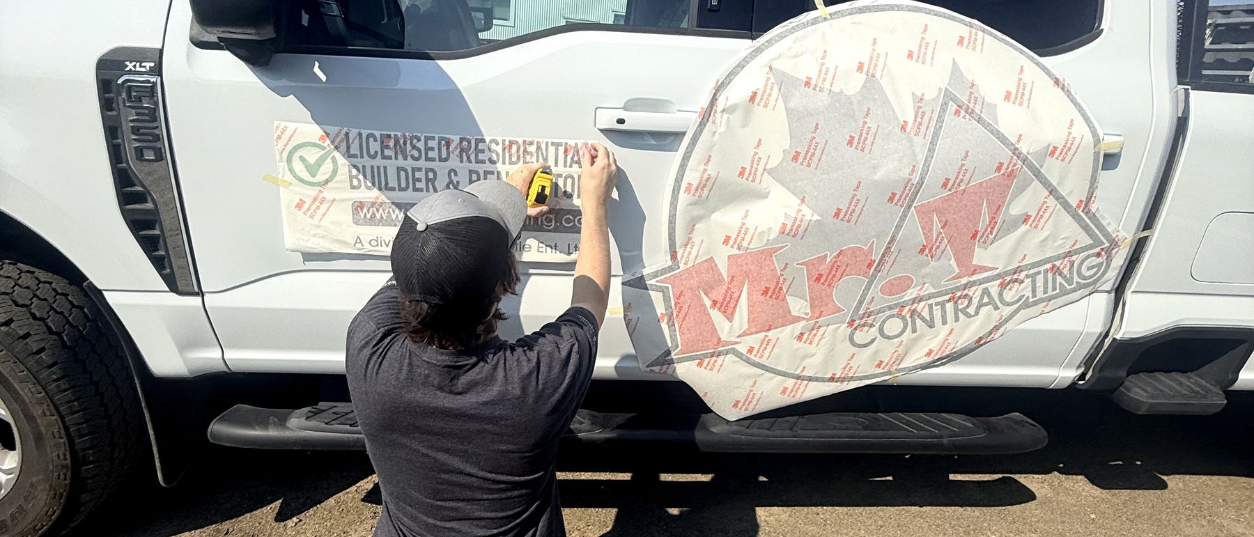 Liam at a truck door, squaring up a graphic under application tape.