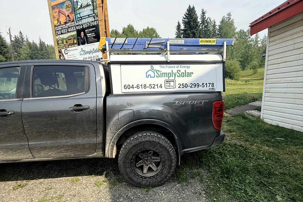 Simply Solar truck parked in front of a Cariboo roadside signboard.