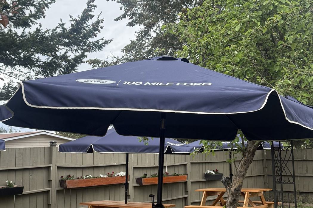 Branded 100 Mile Ford patio umbrellas set up over picnic tables.