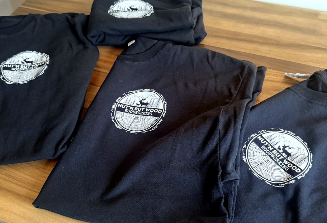 Folded Nut’n But Wood Woodworking tees showing the printed chest badge.